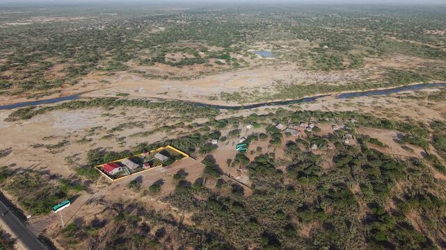 Drone video capturing the vast, arid landscape of La Guajira. The stark terrain, dotted with sparse vegetation and traditional dwellings, is seen under clear skies.