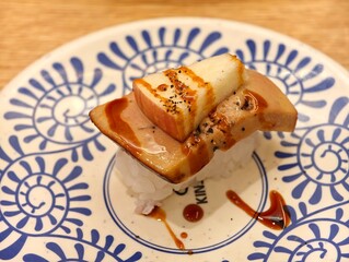 Close-up of a foie gras nigiri sushi topped with a slice of apple and sauce on porcelain plate © Robert