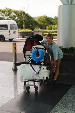 Happy woman laughing next to overpacked luggage cart outside airport