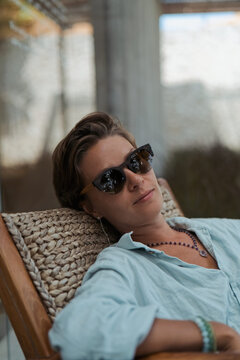 Calm mature woman wearing sunglasses relaxing in rattan chair outdoors