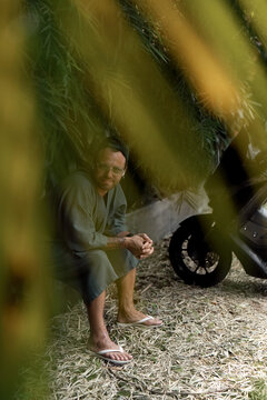 Man sitting near scooter in tropical garden seen through leaves
