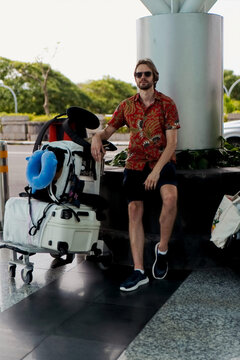 Man traveler in batik shirt waiting at airport with luggage cart