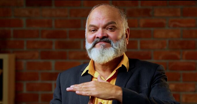 Indian senior businessman or corporate executive gesturing a time out with his hands signaling for a break or a stop in proceedings while standing against a red brick wall in a cozy moody office