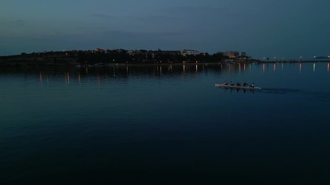 Predawn Crew Pushing Steady Sprint With City Lights Glimmering On Water, Cool Early Tone And Urban Silhouette