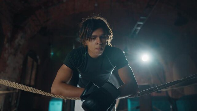Tired boxer resting after hard workout on boxing ring, portrait of black guy. Fighter breathing hard and restoring strength after training in gym, professional sport and hobby for good body conditions