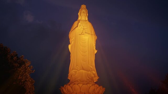 Majestic Golden Lady Buddha Statue Illuminated Against Dark Blue Sky with Low Angle view and Spiritual Tranquility Concept