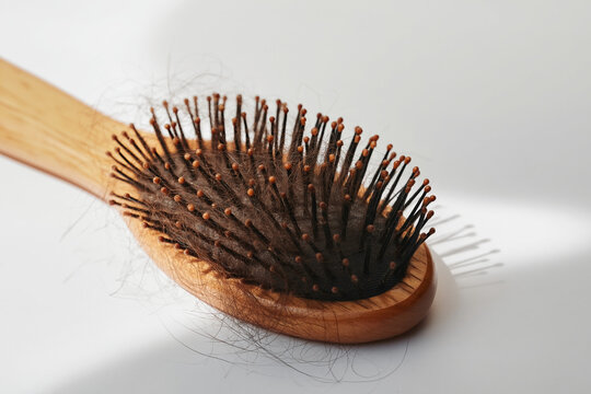 Hairbrush with loose strands of fallen hair rests on a bright clean white background.
