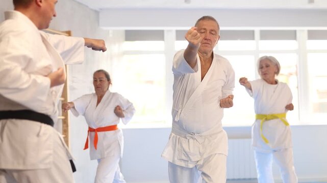 Active mature man wearing kimono training karate techniques in group during workout session