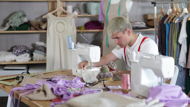 Attentive young male dressmaker working with sewing machine in tailor's workshop