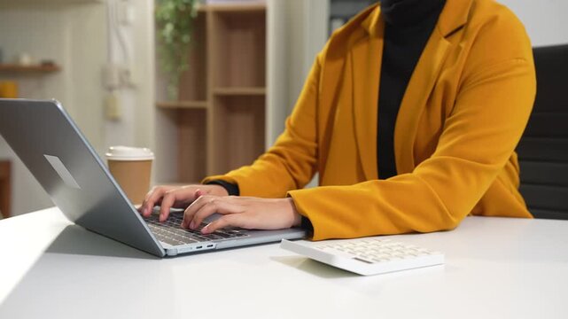 Employee, taking notes sitting at desk using smartphone and laptop searching for information at work.