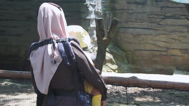 Woman at a zoo with child, observing animals behind a fence. Perfect for illustrating family outings, wildlife conservation, and education.