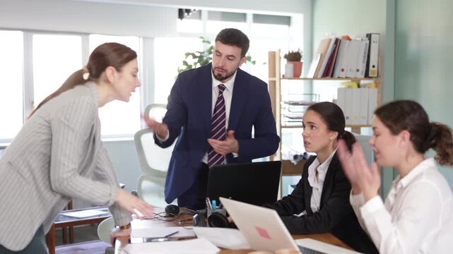 Group of young women and man around table engaged in heated argument in tense office environment