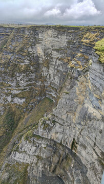 Impresionante vista vertical de un precipicio rocoso con estratos visibles y vegetaci&oacute;n escasa. El abismo muestra la magnitud de la geolog&iacute;a bajo un cielo nublado y atmosf&eacute;rico.