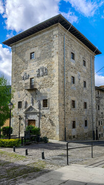 Imponente torre medieval de piedra con escudos her&aacute;ldicos, portal labrado y balcones, bajo un cielo azul con nubes. Un ejemplo majestuoso de arquitectura hist&oacute;rica y patrimonio cultural.