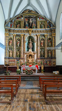 Interior de una iglesia con un retablo barroco dorado, esculturas religiosas y bancos de madera. El altar est&aacute; decorado con flores en un ambiente de devoci&oacute;n, silencio y patrimonio hist&oacute;rico.