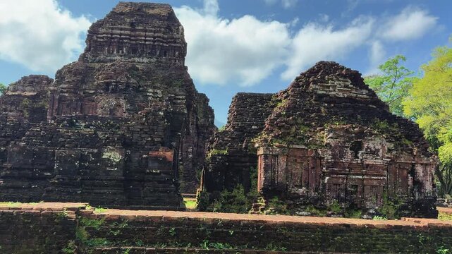 Ancient Cham temple ruins at My Son Sanctuary near Hoi An, Vietnam. Moss-covered brick towers stand beneath blue sky, showcasing centuries of Hindu architecture and Southeast Asian history.