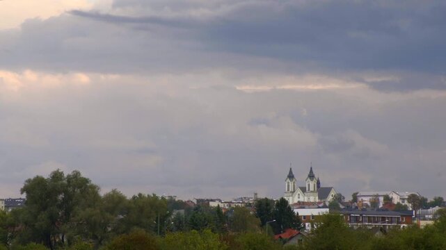 Time lapse of distant church towers and low buildings above suburban landscape under dynamic cloudy sky. Sanok city, Poland.