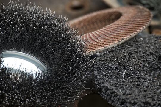 Abrasive tools including wire wheel, flap disc, grinding wheel on workshop surface showing texture