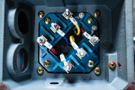 Internal view of an industrial electric motor terminal box, showing three-phase wiring connections with yellow markers (W2, U2, V2, V1) and copper jumpers on an orange terminal block