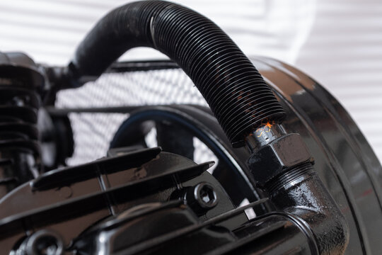 Close-up of a two-cylinder belt-driven air compressor pump mounted on a blue tank, featuring large air intake filters, cooling fins, and a protective wire mesh guard over the flywheel