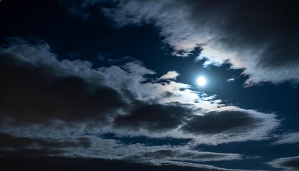 Obraz premium Glowing nearly full moon backlighting layered clouds at night, showing silver linings and halo