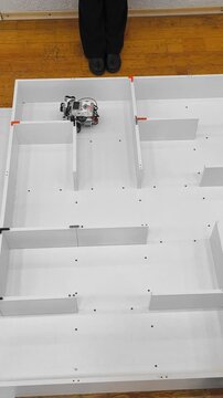 An autonomous robot moves through a maze of partitions, developing algorithms for pathfinding and navigation in robotics.
