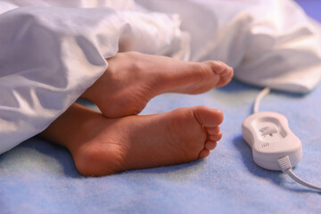 Fototapeta premium Little girl's feet lying under blanket on electric heating pad in bedroom at night, closeup