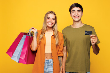 Naklejka premium Young couple two friends family man woman wears casual clothes hold paper package bags after shopping credit bank card together isolated on plain yellow background. Black Friday sale buy day concept.