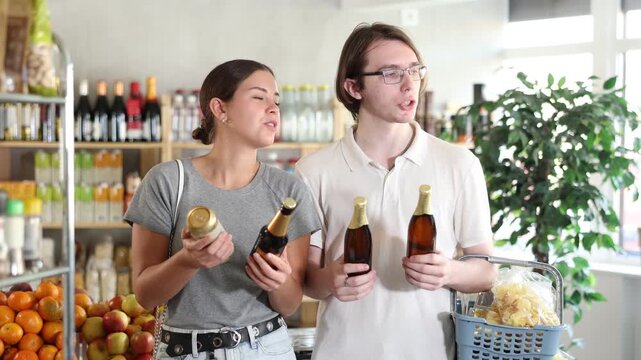 European friends took some varieties of beer from shelf, chooses products. Clients guy and girl compare glass and tin beer package, doubt and make purchase decision