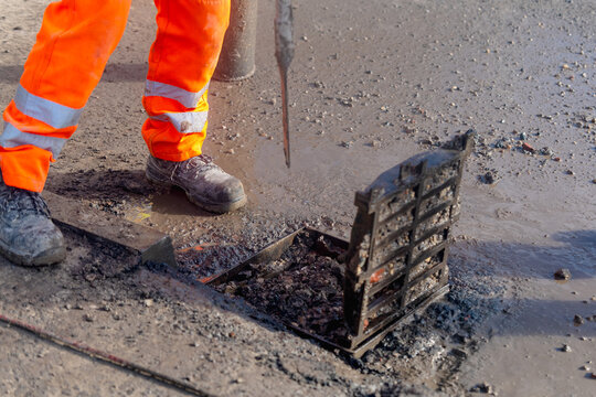 Worker clears debris from a storm drain during road maintenance work in the daytime