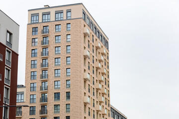 Fototapeta premium Modern apartment building stands tall against gray sky. Windows reflect city's quiet hum. Balconies offer views and everyday life. Clean lines suggest urban comfort