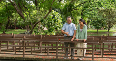 Fototapeta premium Smiling senior man and young woman having romance love conversation dating outdoors in greenery nature. Happiness age gap couple enjoying date relationship and talking together in public park.