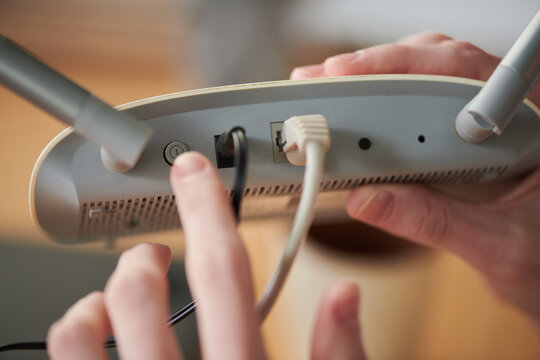 Close up of adult hands connecting cables to wireless router, pressing power button for internet setup and home network installation. Useful for broadband, tech support, connectivity ads