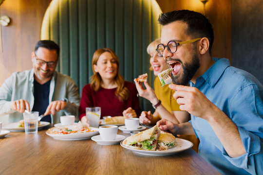 Man eating sandwich with friends enjoying meal together in cafe