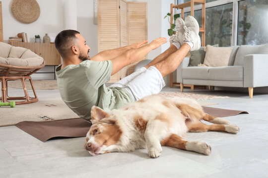 Sporty young man with Australian Shepherd dog training on mat at home