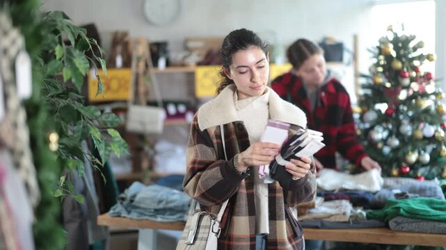Armenian woman stands in a store decorated for Christmas and New Year and chooses a set of warm socks. Woman choosing socks for Christmas gift for friends. High quality 4k footage