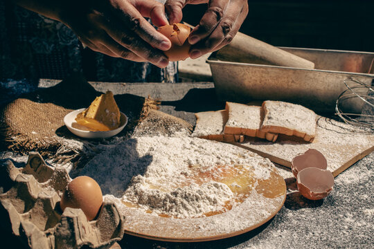 Close up of a woman hands cracking a fresh egg into white flour yolk falling, preparing homemade rustic bread dough in a traditional kitchen, lifestyle baking process concept. 