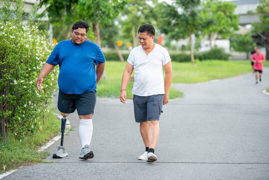 Caregiver assisting and taking care of disabled man with prosthetic leg outdoors. Supportive friend caring for male amputee with artificial limb near public stairs in urban.