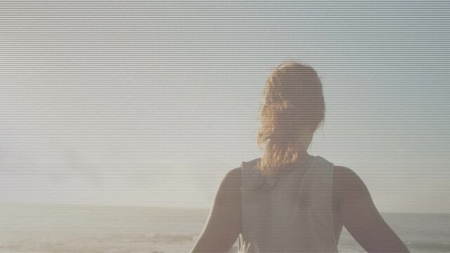 Vertical video: Woman responding to low sun, doing cyclical arm stretches facing ocean for wellness