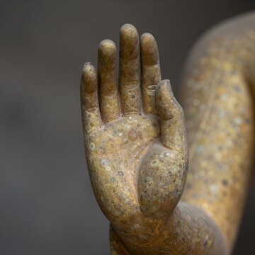 Close-Up of Buddha's Hands in Vitarka Mudra Against Textured Stone