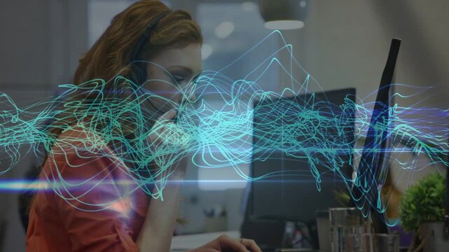 Support agent receiving call, typing and jotting notes for help while waveform overlaying monitor