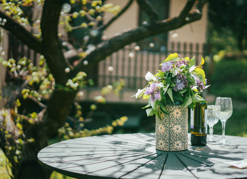Romantic summer table setting in garden with lilac flowers, wine bottle and glasses