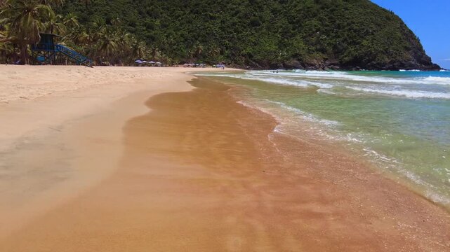 POV walking along the shore of the large beach in Choroni, Aragua, Venezuela, on a sunny day with clean sand and crystal-clear water