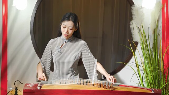 Art, creative and performance with woman expertly musician deeply engaged in playing traditional musical stringed instrument Chinese zither or guzheng, highlighting artistry, dedication to music