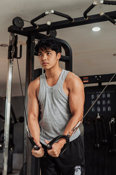 Young Asian man does cable crossover at the gym, focusing on chest development, muscle activation, and controlled movement for upper body strength training.