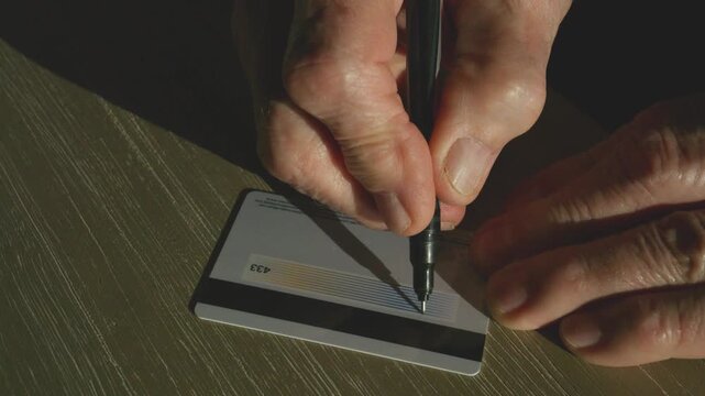 senior citizen signing the back signature strip on a credit card (fake credit card)