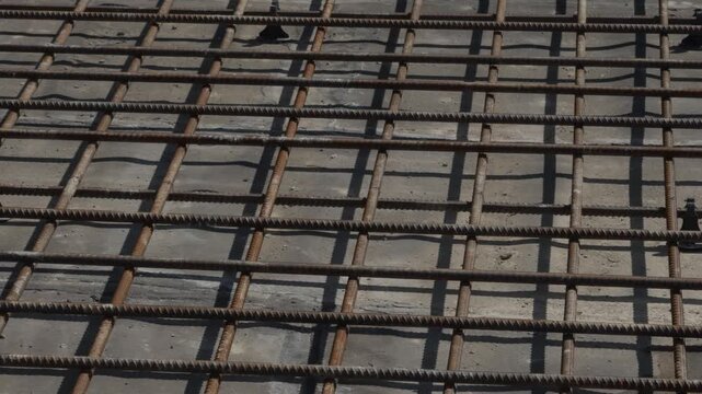 Top view of a grid structure formed by steel rebars with a corroded surface and plastic spacer elements, prepared before concrete pouring. Rough construction and engineering.
