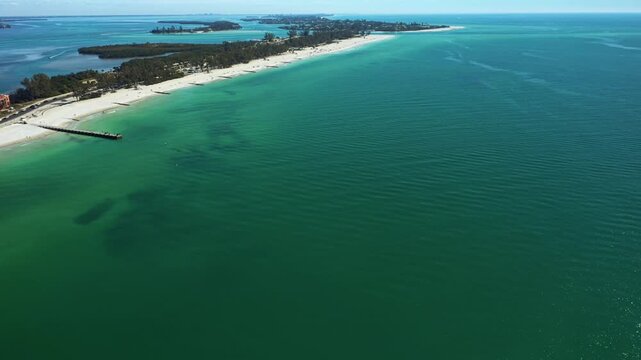 A serene stretch of Bradenton Beach with calm emerald waters and a distant pier.