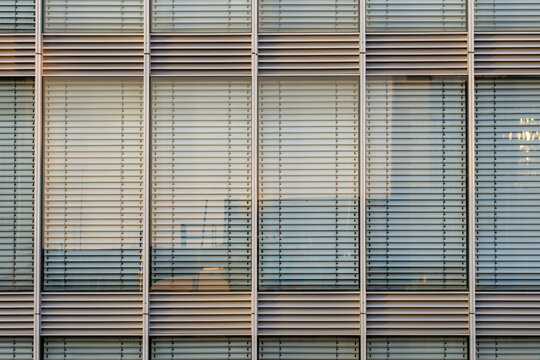 Glass windows with blinds on modern office building facade create rhythmic lines pattern and architecture texture for minimal abstract design background