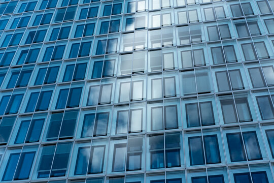 Blue glass windows on modern office building facade create a strict grid pattern with architecture symmetry and abstract texture background
